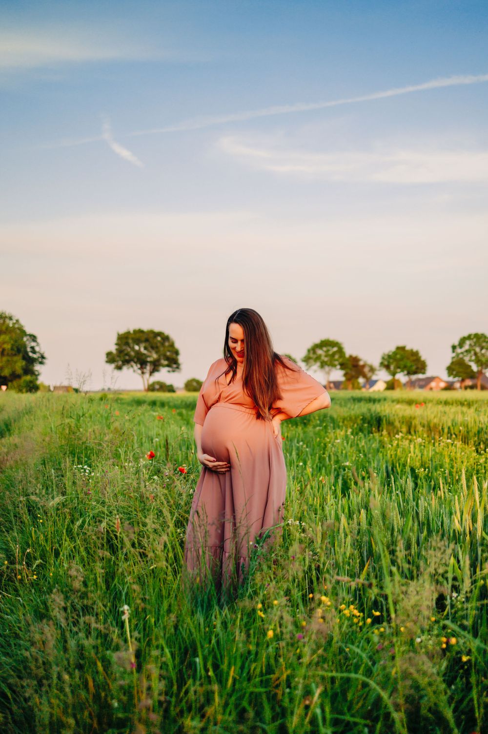 A woman in a pink dress stands in a lush green field during golden hour.