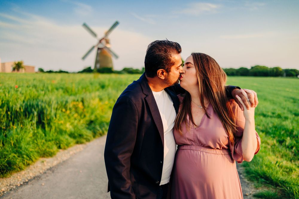 A tender moment captured between a couple on a country path with a windmill behind them.