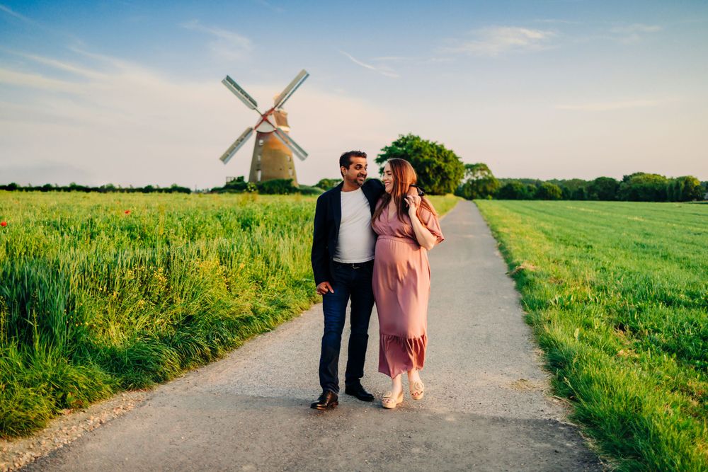 A couple walking down a path through green fields with a windmill in the distance.