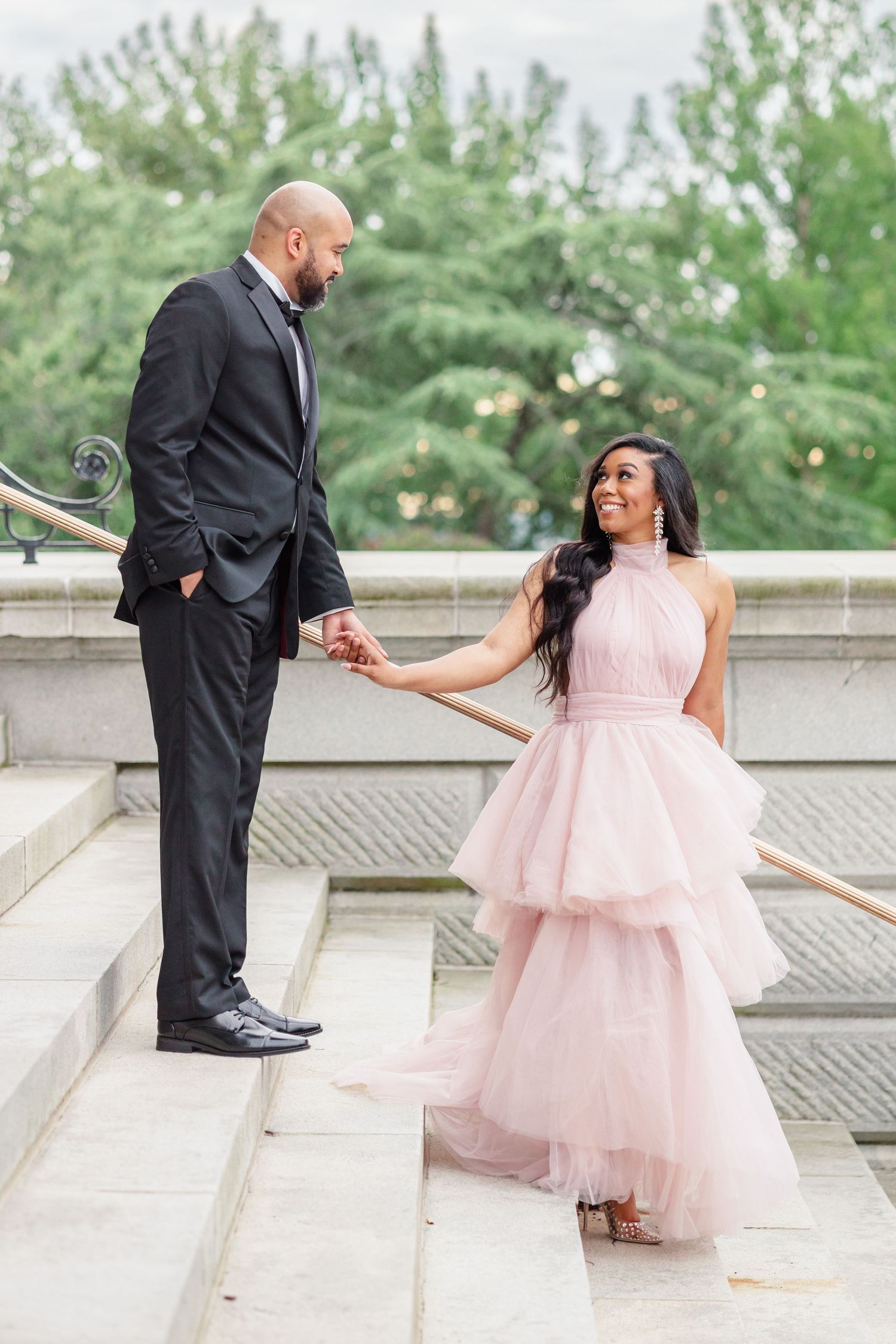 Couple shares romantic moment on marble steps, with her pink layered gown flowing beautifully.