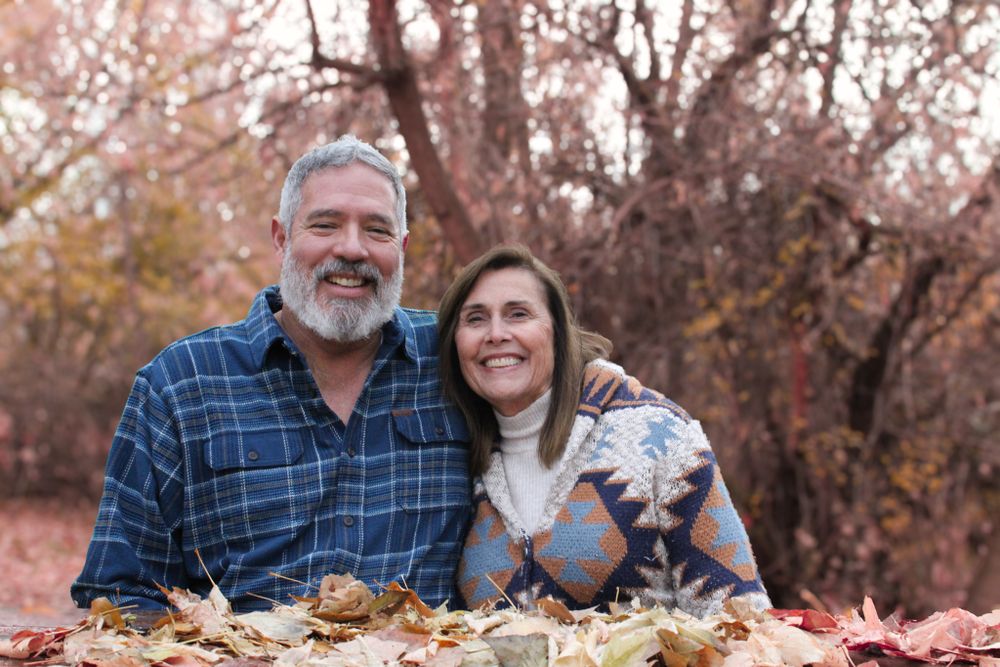 Couple sitting together in fallen autumn leaves wearing matching plaid clothing.