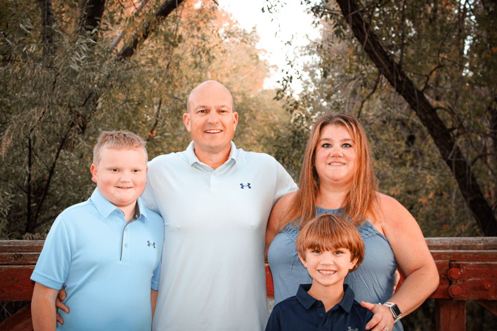 A family of four poses outdoors for a portrait against a backdrop of autumn trees and foliage.