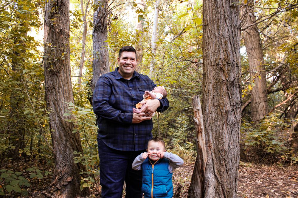 Outdoor autumn family portrait between tall trees in the forest.