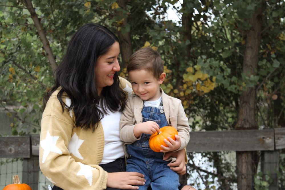 Mother and child holding small orange pumpkin during fall photo session outdoors.