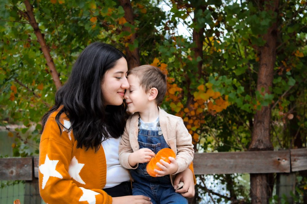 Sweet autumn portrait with small pumpkin against colorful fall foliage background.