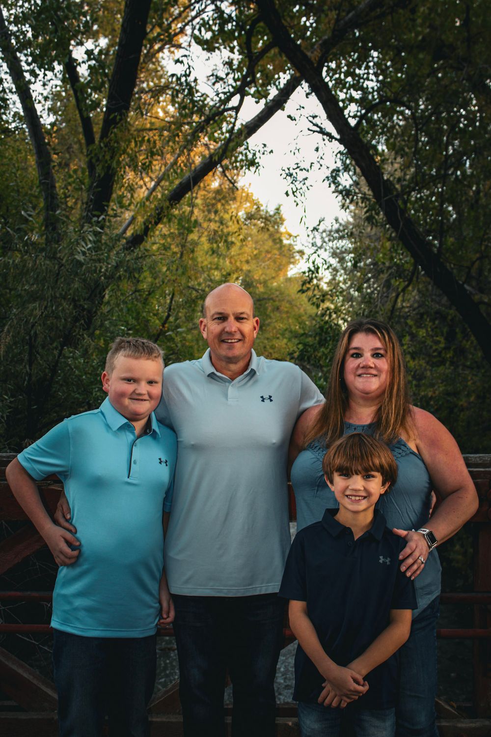 Family portrait taken at sunset on a wooden bridge surrounded by autumn trees.