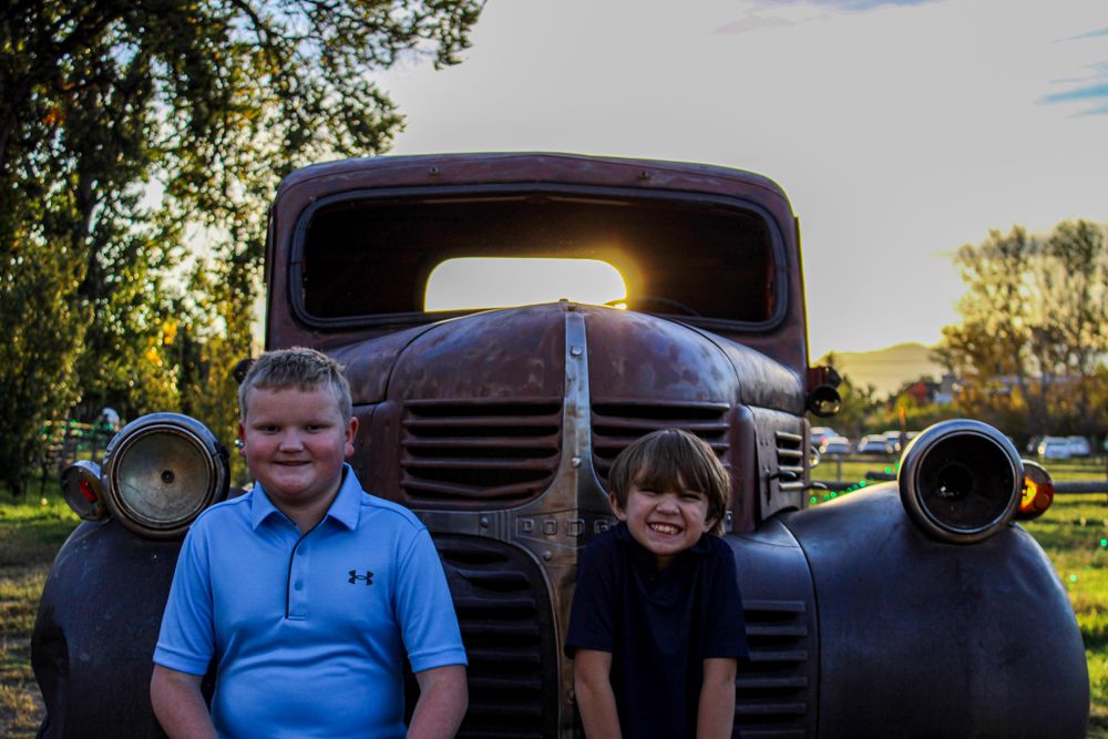 Two children posing in front of vintage truck during sunset.
