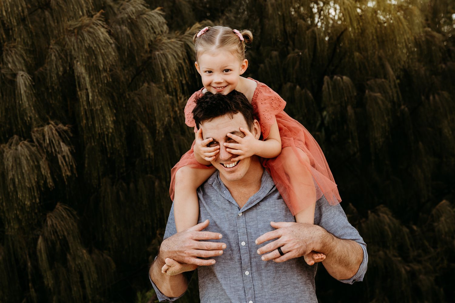 A playful piggyback ride moment captured in front of lush greenery.