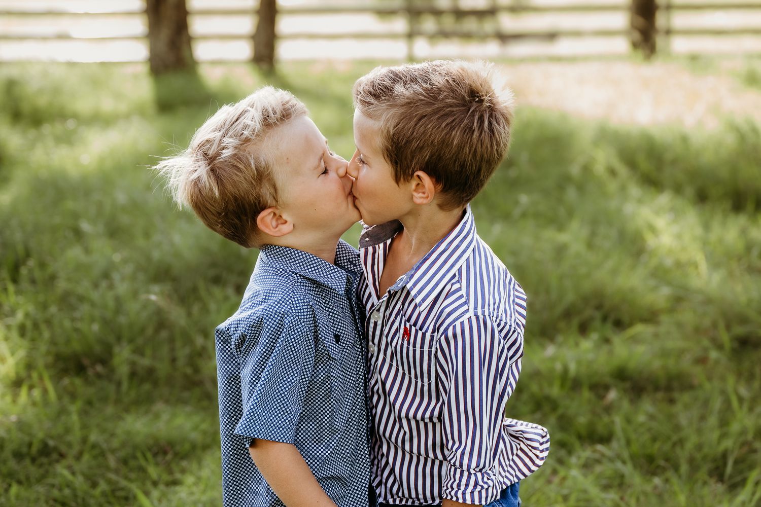 Two children share an innocent moment in a sun-dappled green field.