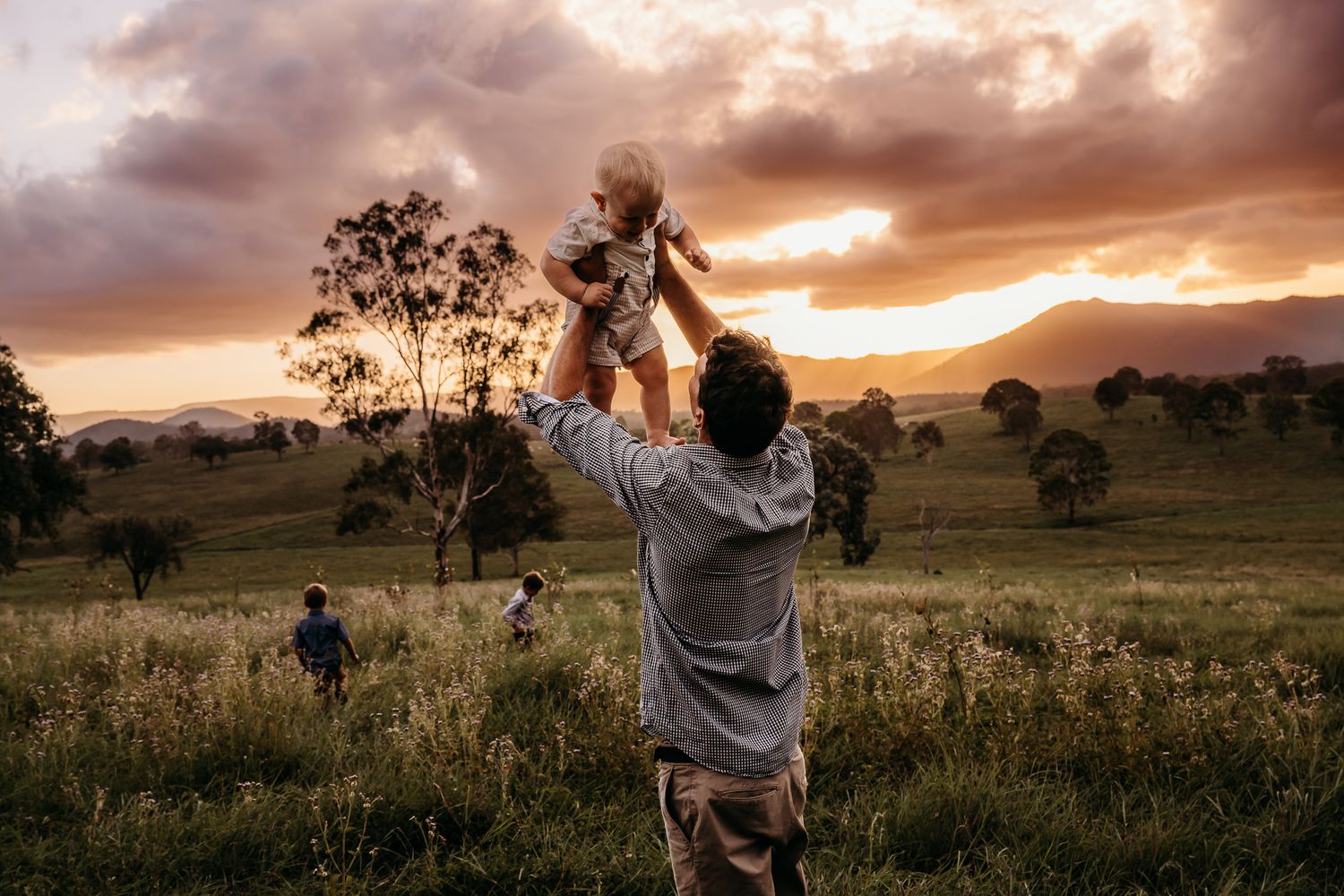 People enjoying playful moments in a scenic field during golden hour with mountains in the distance.
