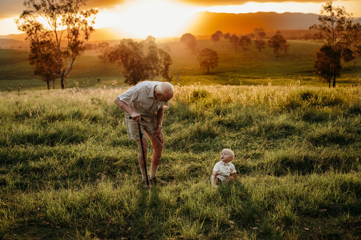 Two figures playing in a sunlit meadow during golden hour with mountains and trees in background.