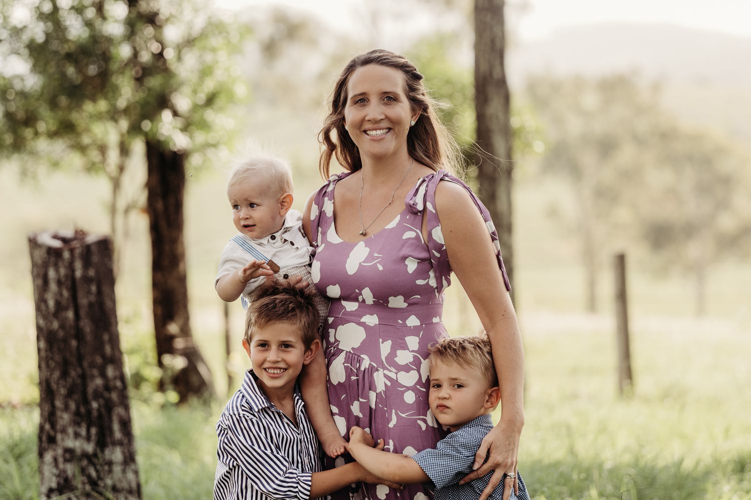 Family portrait in a rustic outdoor setting with trees and natural lighting.
