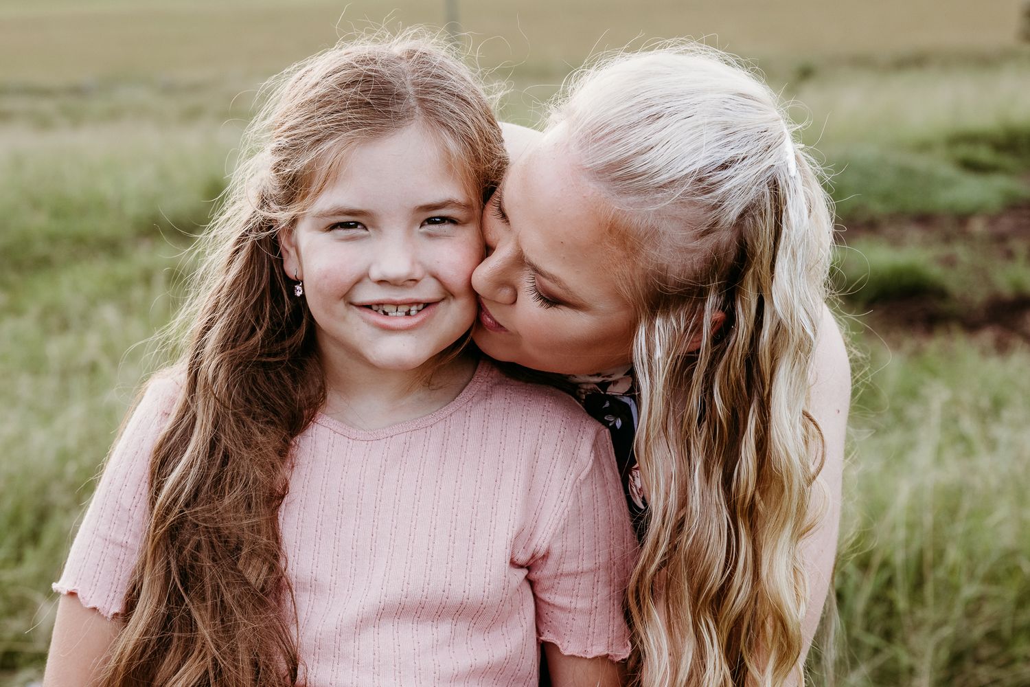A heartwarming moment of affection shared outdoors with pink clothing and long hair.