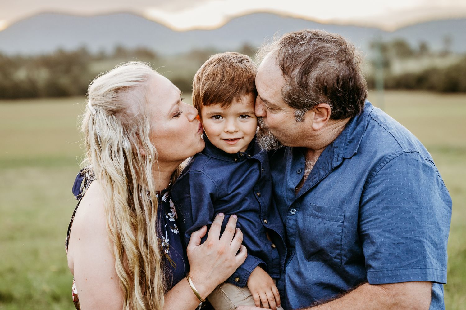 A loving family moment captured outdoors with mountains in the background.