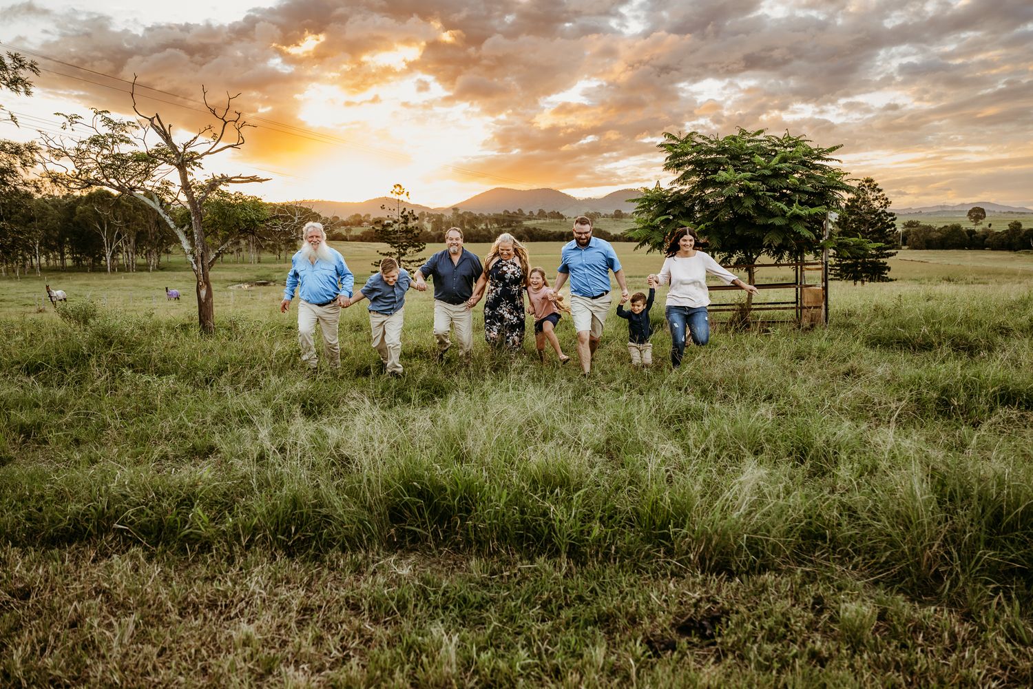 A group runs joyfully through a grassy field at sunset holding hands.