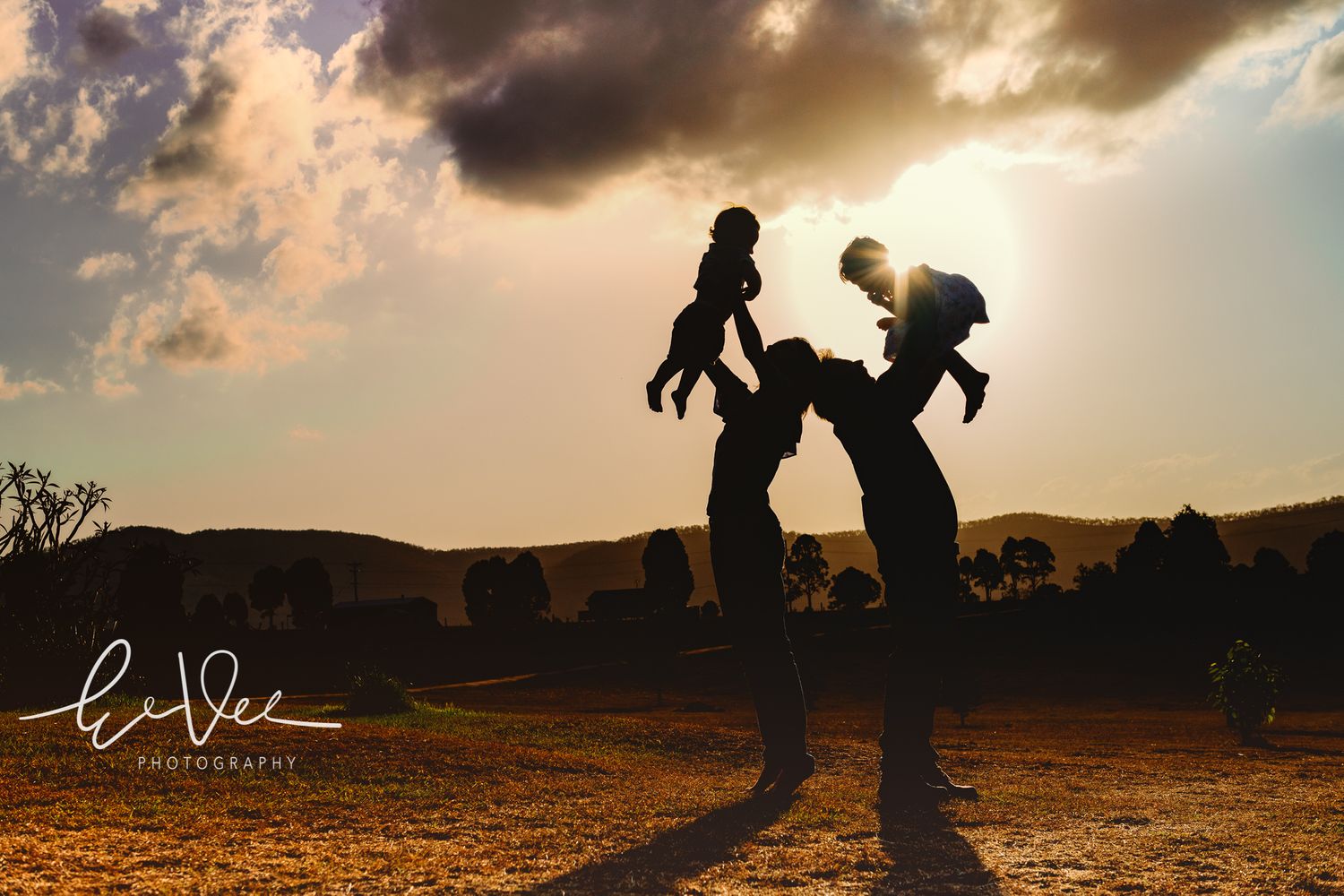 Silhouettes playing and lifting children against a dramatic sunset sky.