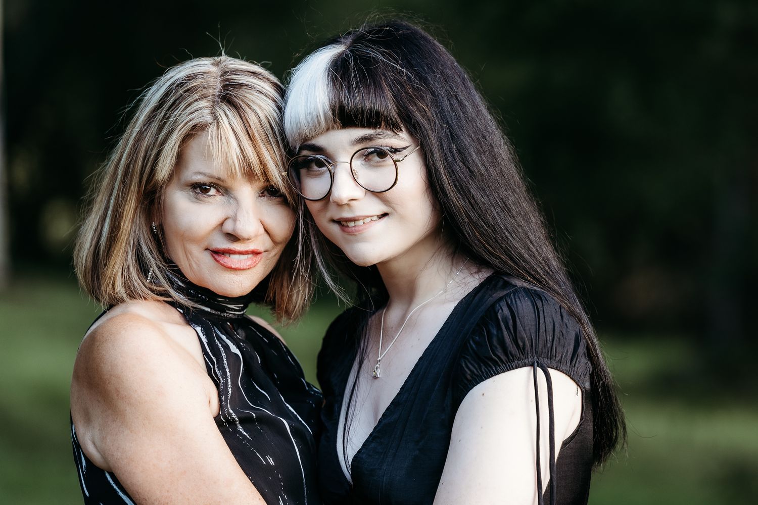 Two people in black outfits posing together in outdoor portrait.