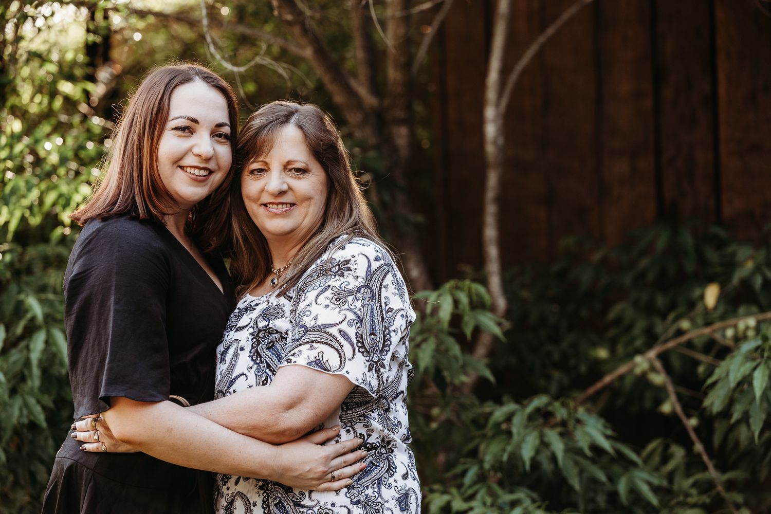 Two people embracing in casual portrait against wooden background.