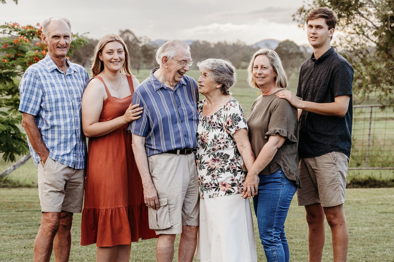 Multi-generational family gathering outdoors for a portrait in casual summer clothing.