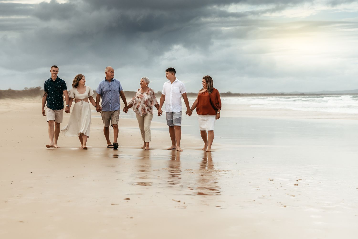 Group walking together along a peaceful beach shore under dramatic storm clouds.