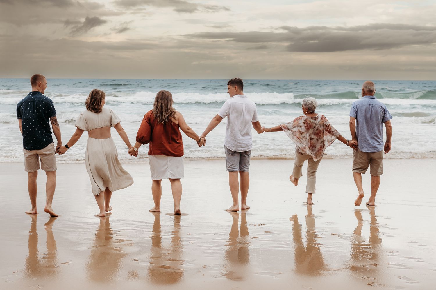 Group of friends holding hands while walking along the beach at sunset.