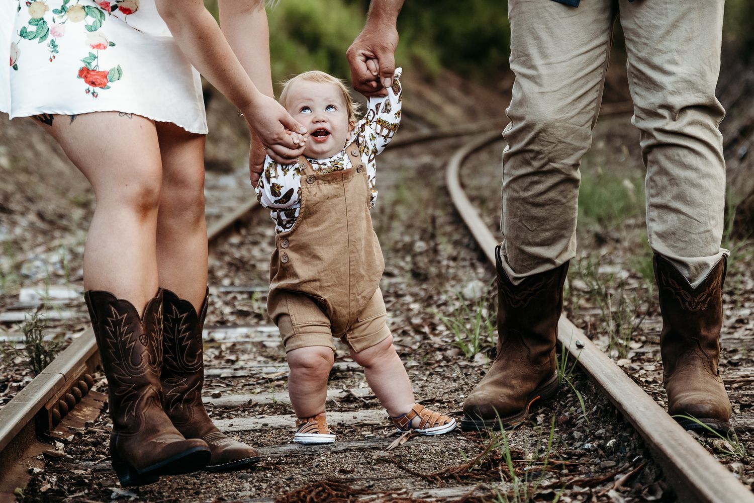 Family feet with boots standing on train tracks in countryside setting.