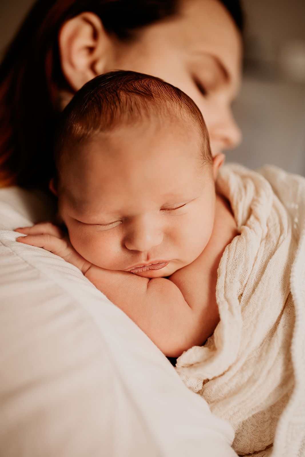 A baby boy rests his head on his mother's shoulder while sleeping peacefully. Oahu Newborn Photographer.