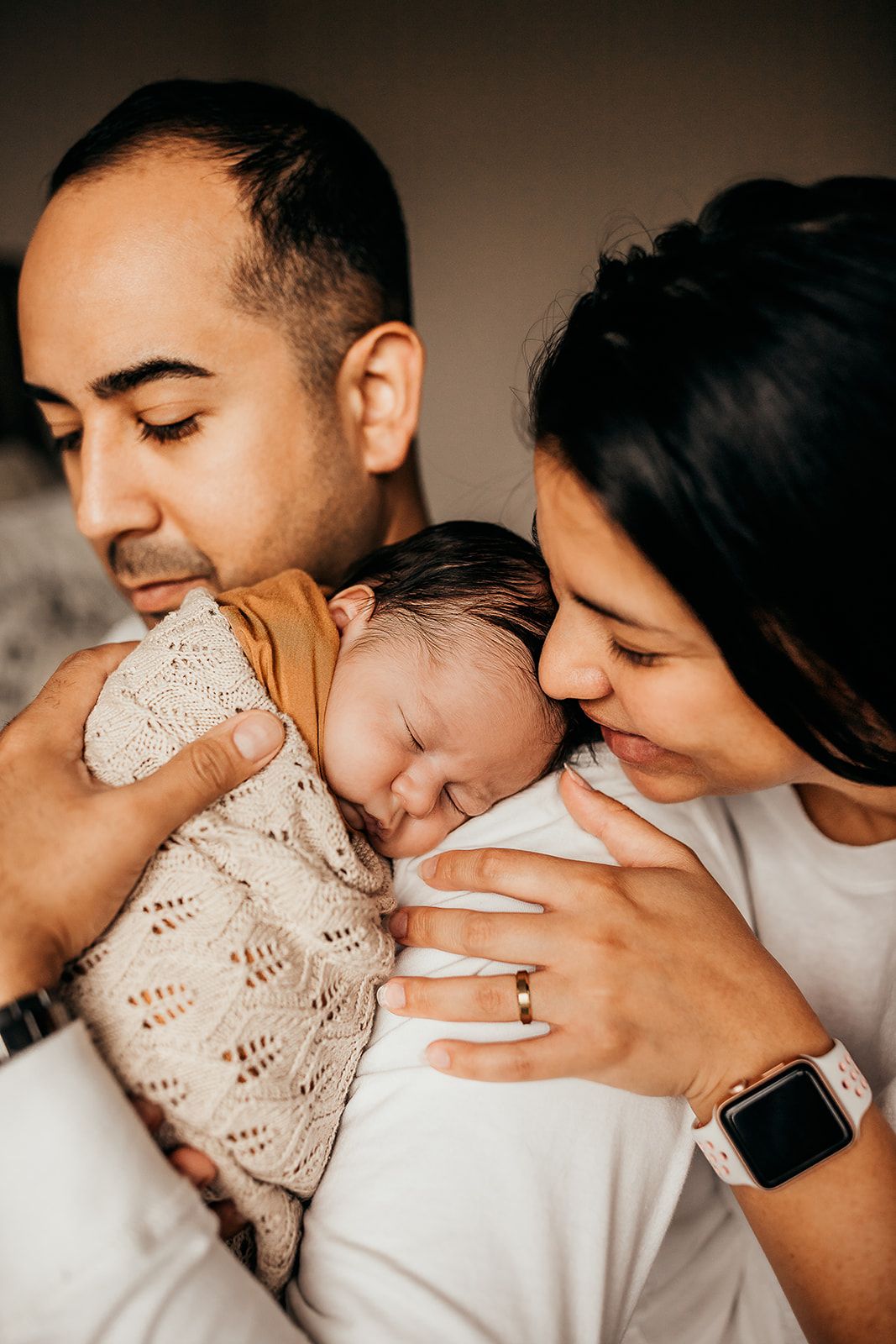 A father holds his son over his should while the mother leans in to nuzzle him. Honolulu Newborn Photographer.