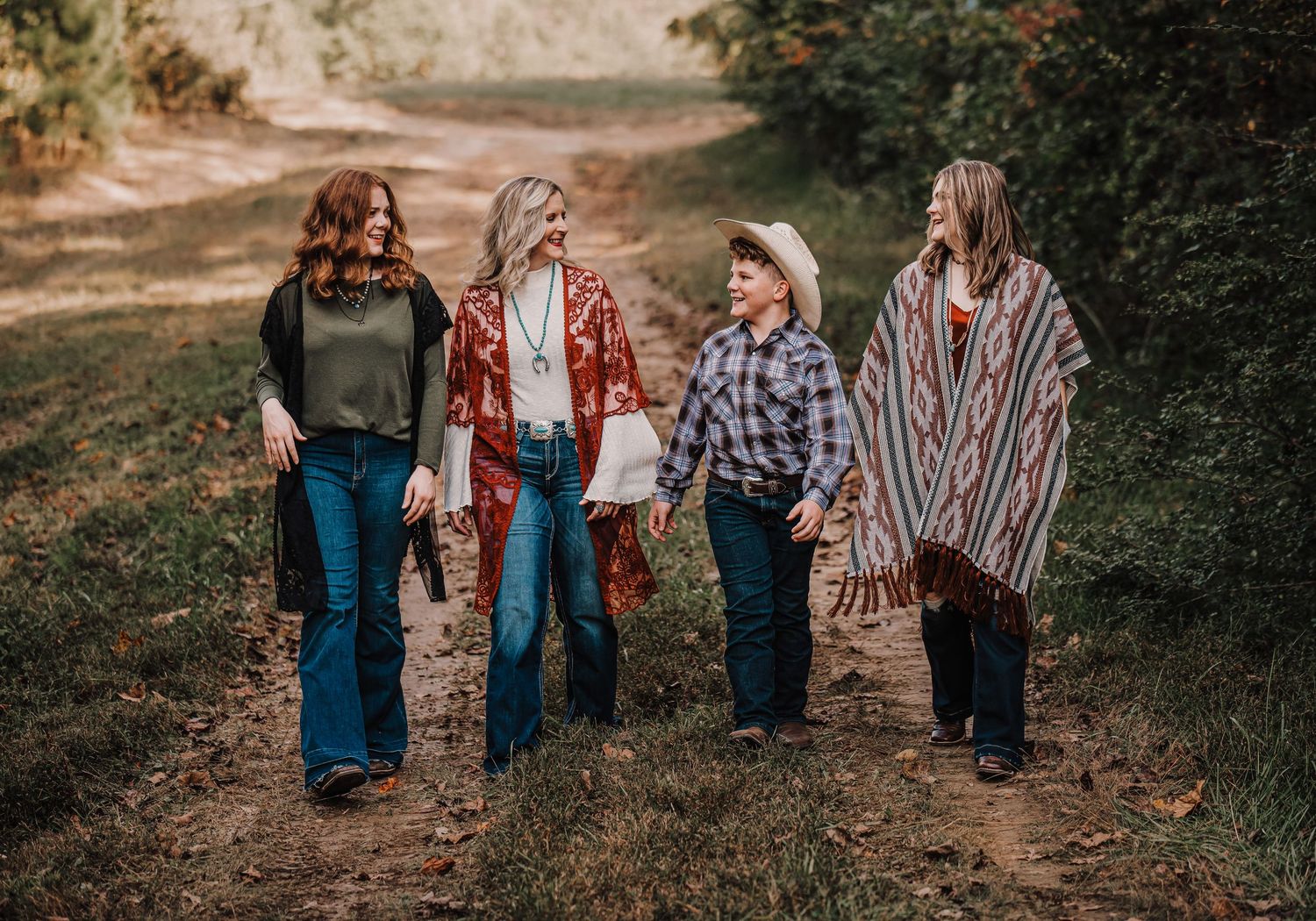 Family walking together on rustic path wearing casual bohemian style clothing.