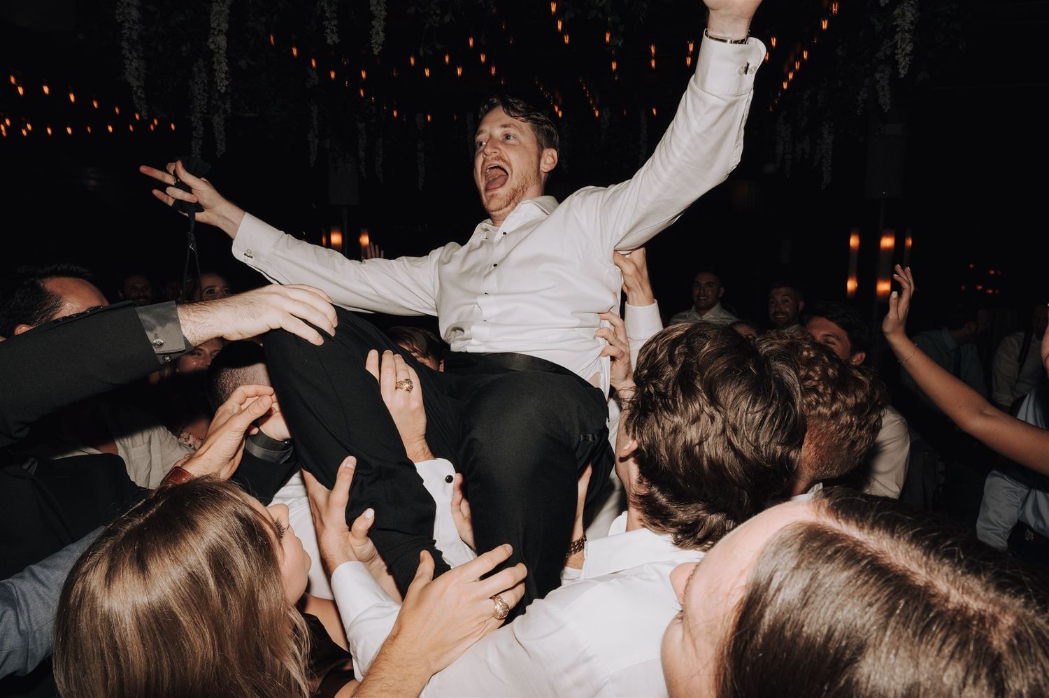 Party guests lift someone up during celebration as crowd cheers below.