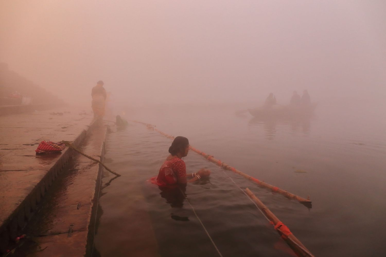 Pilgrims at dawn participating in spiritual ceremonies along foggy Varanasi riverbank.