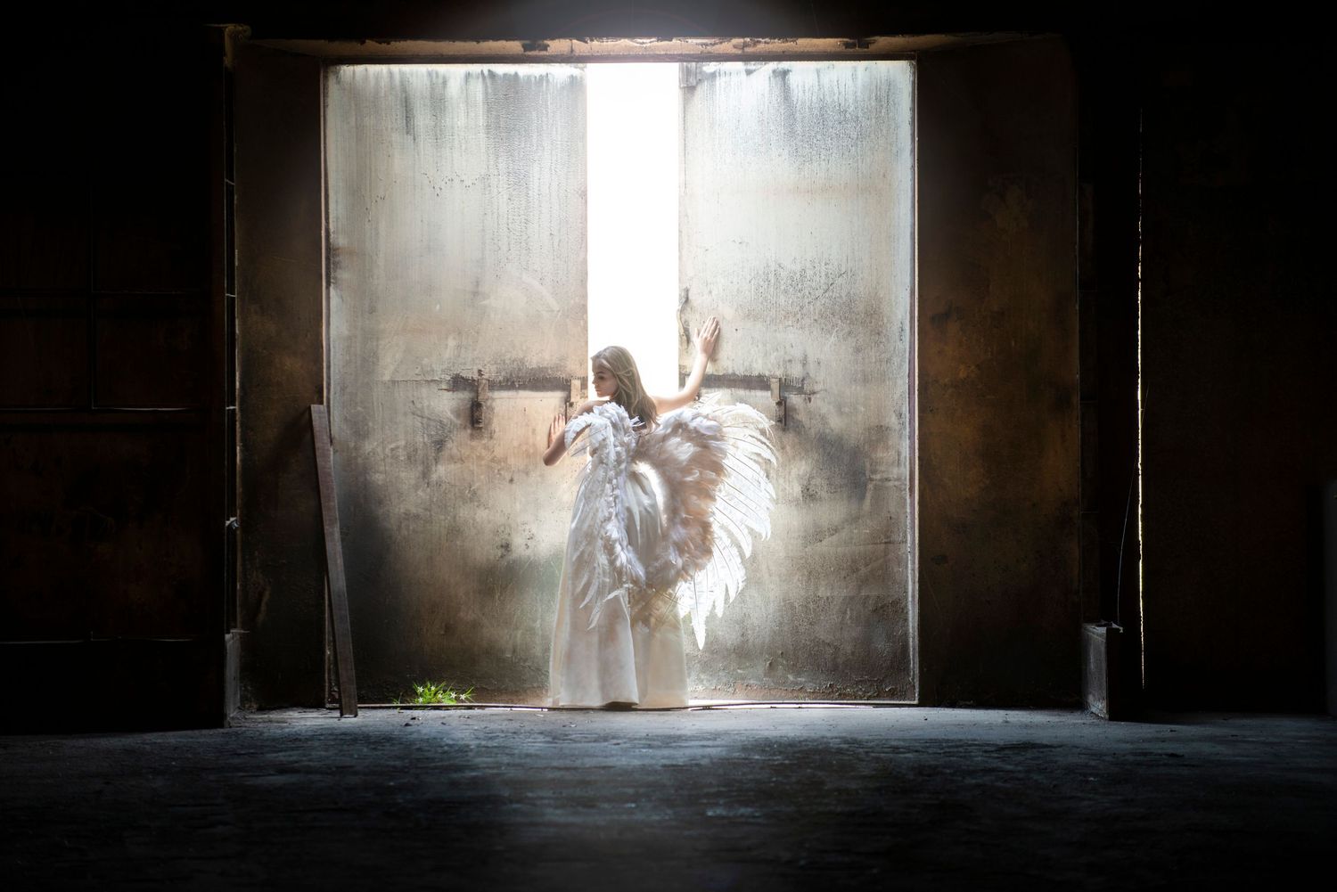 Dramatic silhouette of figure in white dress dancing in sunlit doorway with dust particles.