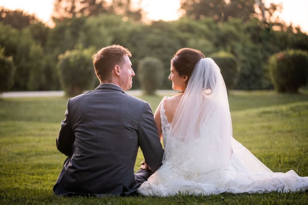 Bride and groom sitting in the grass at golden hour at Stratford Country Club wedding