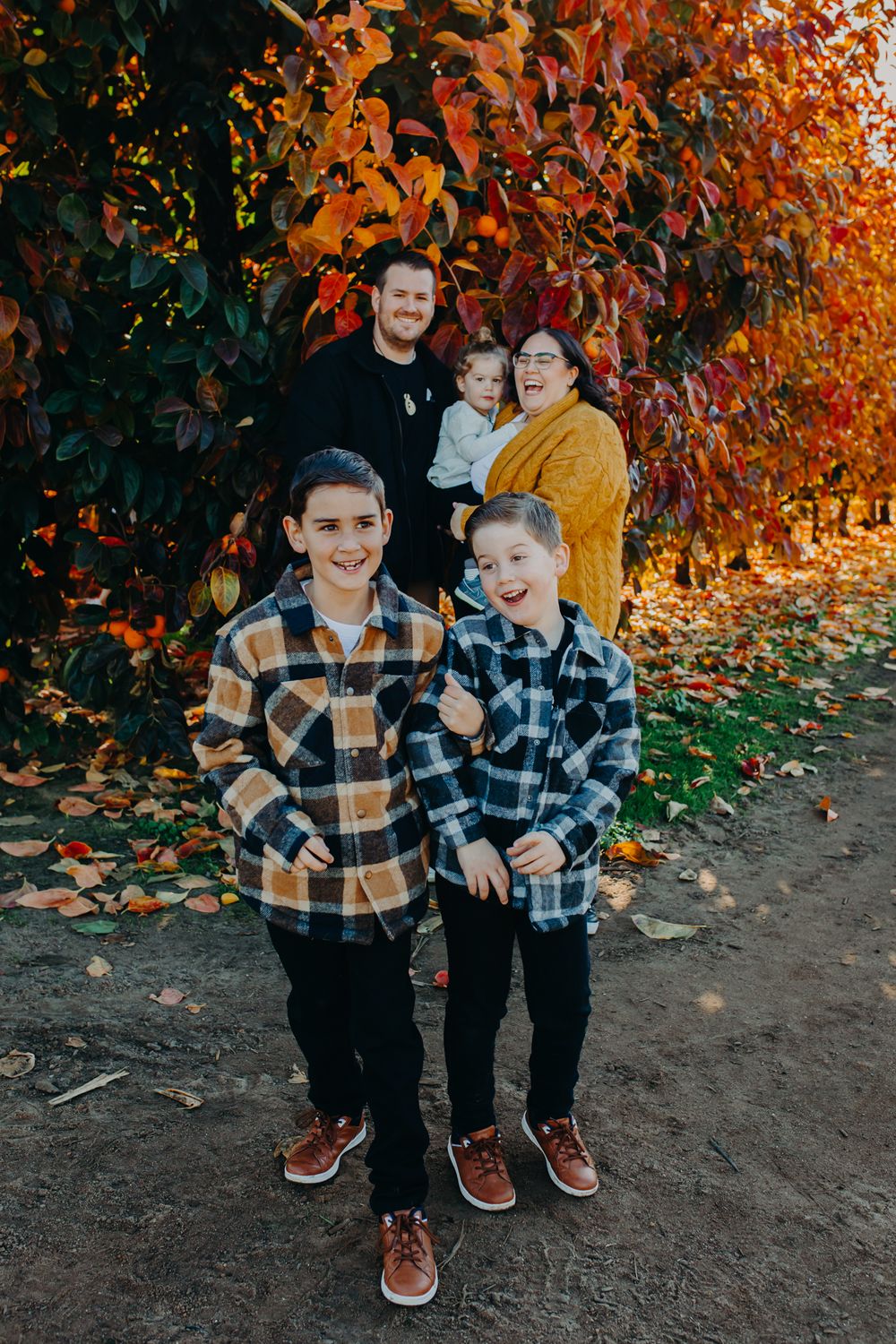 Group wearing plaid flannel shirts poses against vibrant autumn foliage on a dirt path.