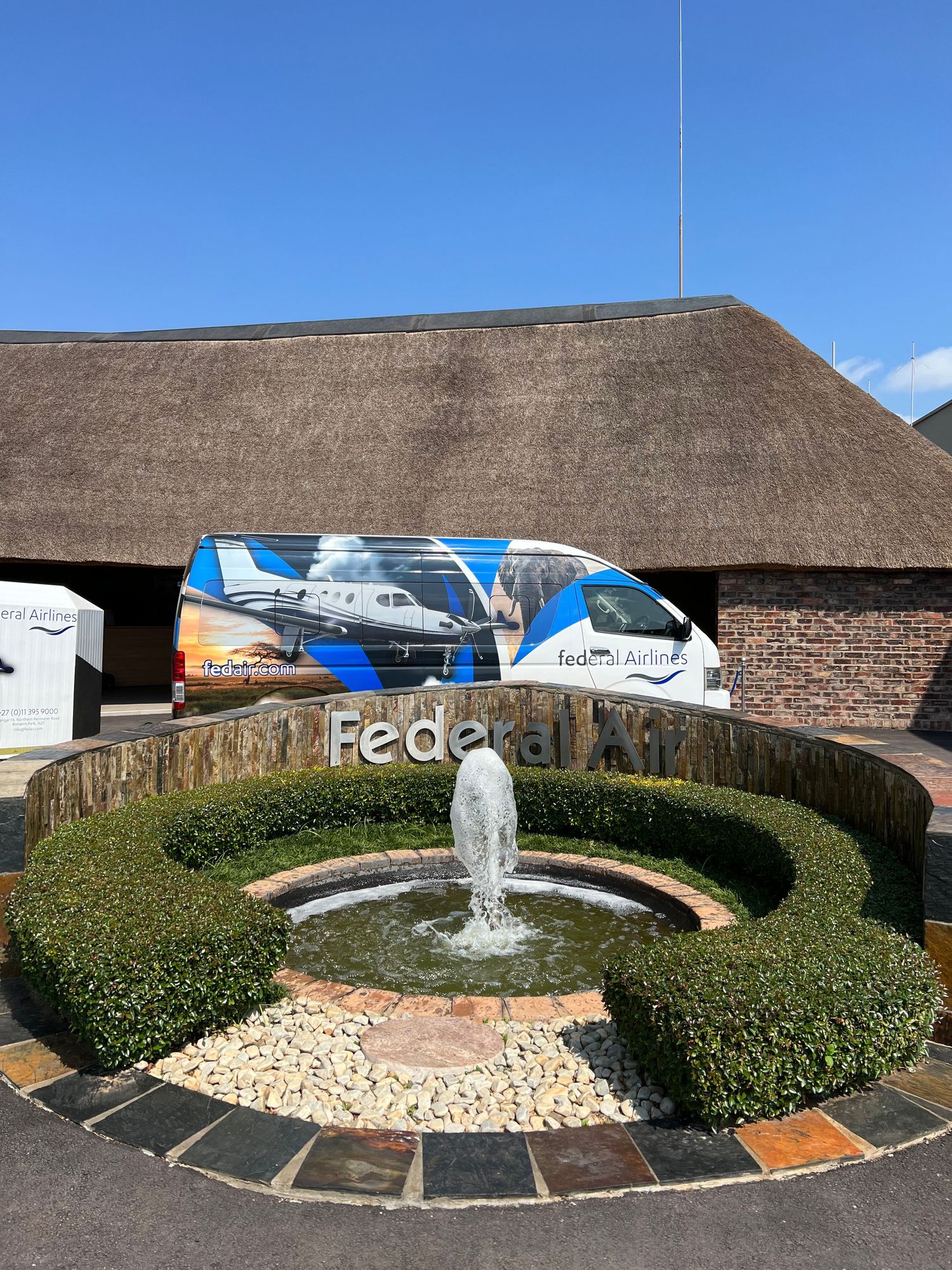 Small aircraft parked in front of circular garden with fountain at Federal Airlines terminal.