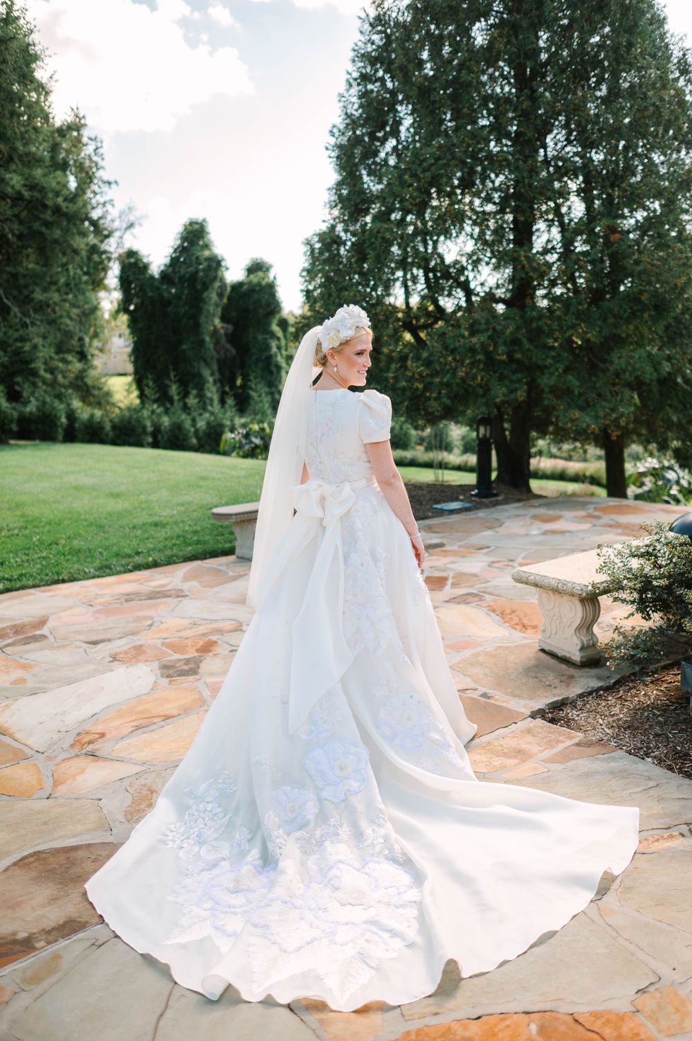 A stunning wedding dress with detailed train photographed from behind in a garden setting.