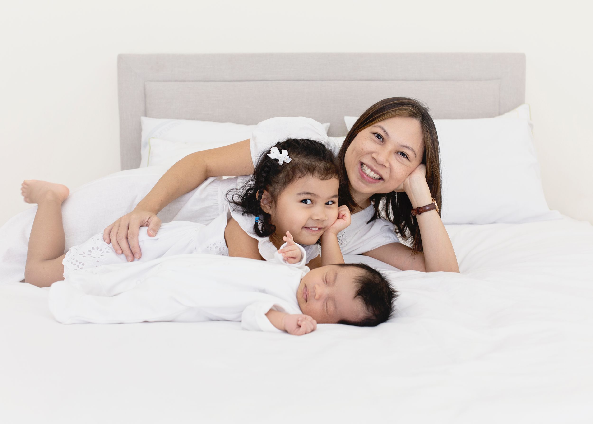 Mom and her two little girls posing on bed for an light and airy Newborn Photoshoot .
