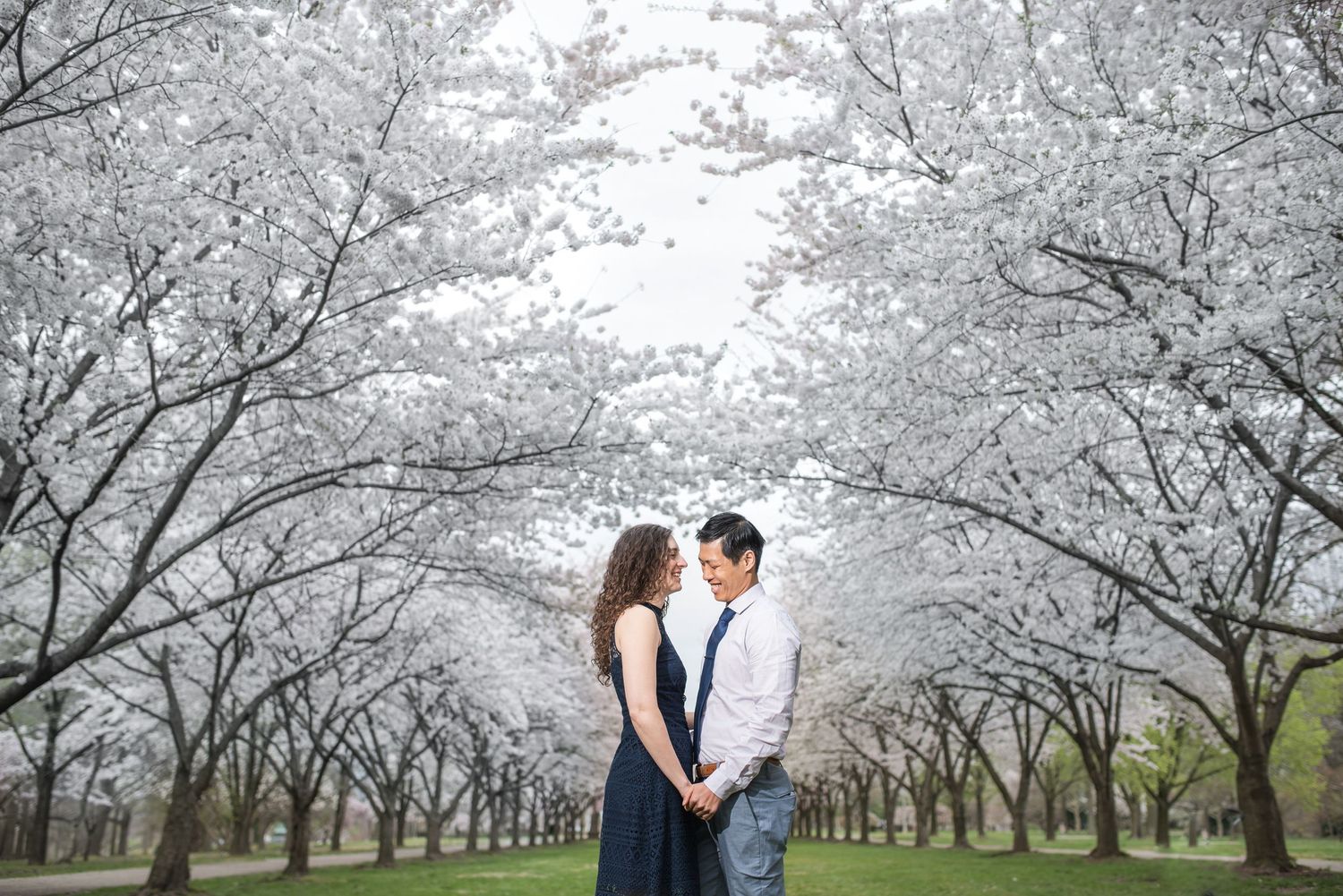 Couple standing together under blooming cherry blossom trees on cloudy day.