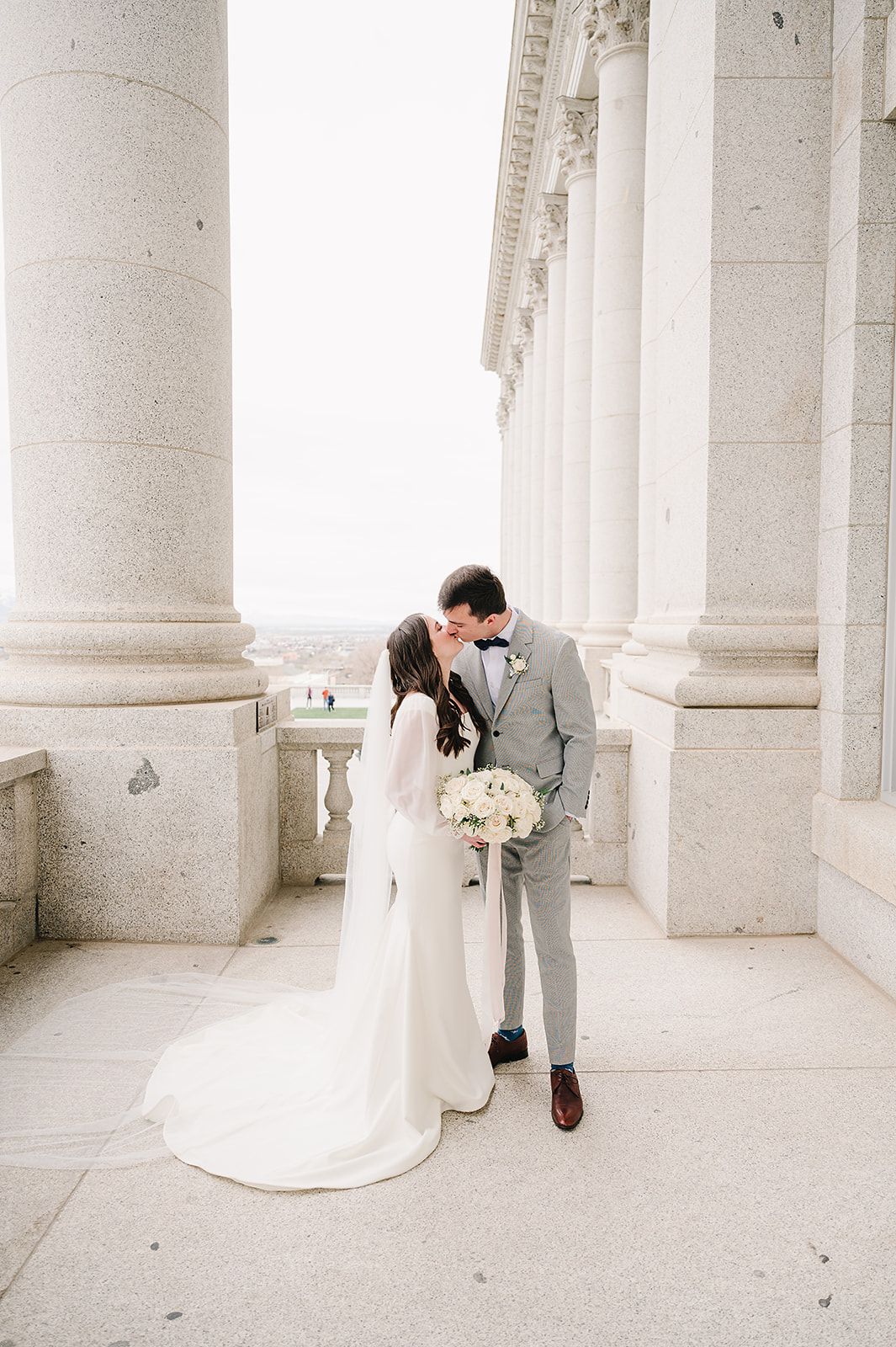 Wedding couple sharing intimate moment between elegant white columns of classical building.