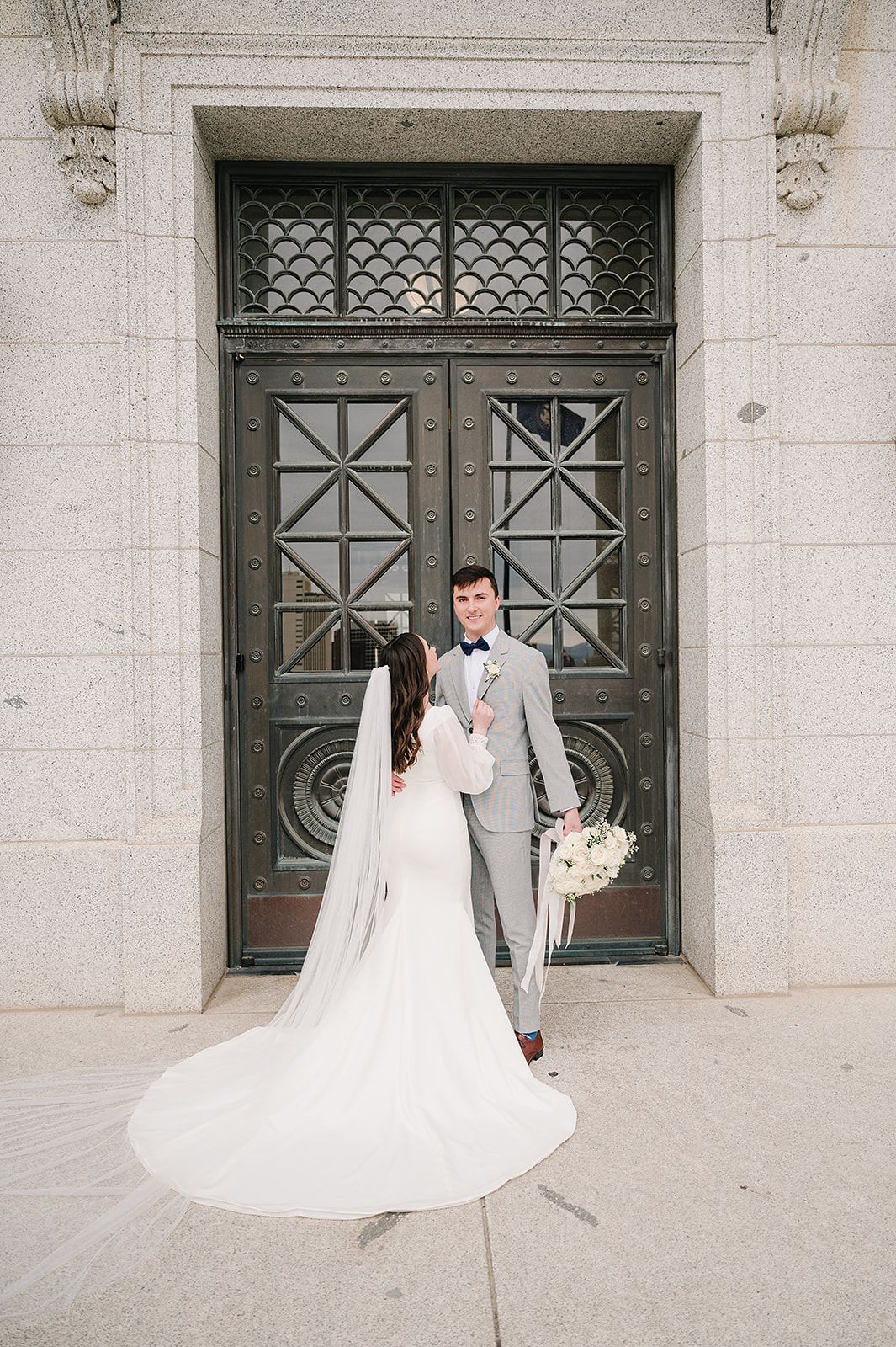 Wedding couple posing in front of ornate metal doors with long flowing wedding dress train.