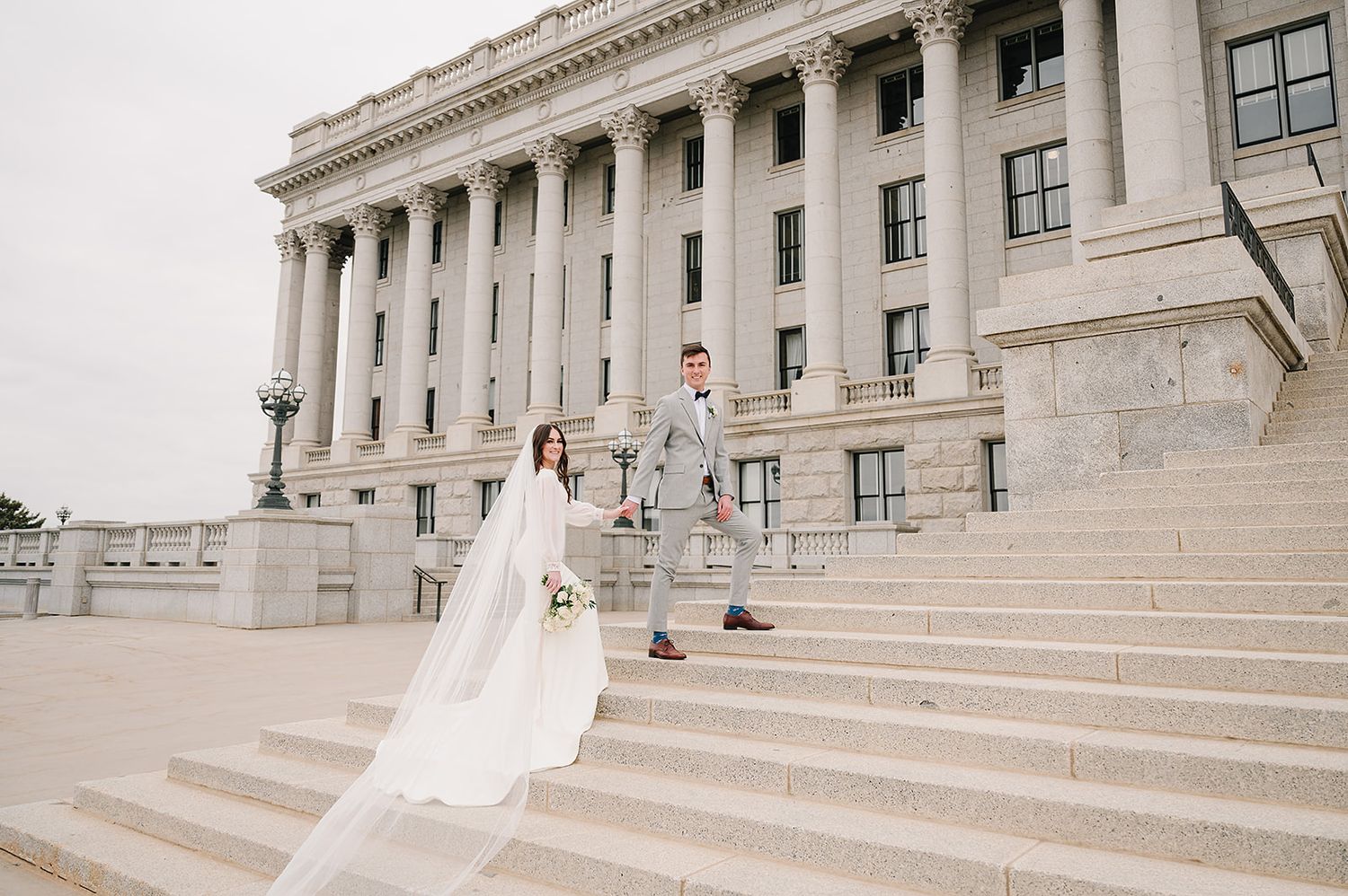 Wedding couple poses on grand stone steps of stately government building with white columns.
