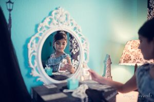 Vintage-style ornate white mirror reflects a vanity scene against a turquoise wall with soft lighting.
