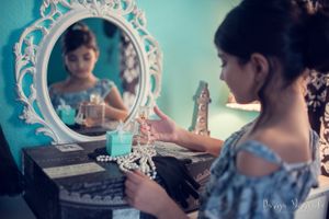 Vintage vanity scene with pearl necklace and jewelry box reflected in white baroque mirror.