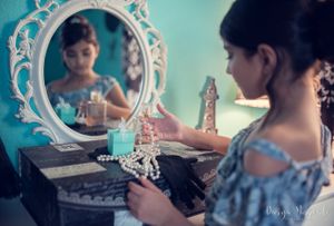 Decorative white mirror reflects delicate jewelry arrangement on dark vanity against turquoise wall.