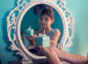Small tiffany blue gift box reflected in ornate white mirror with turquoise wall background.