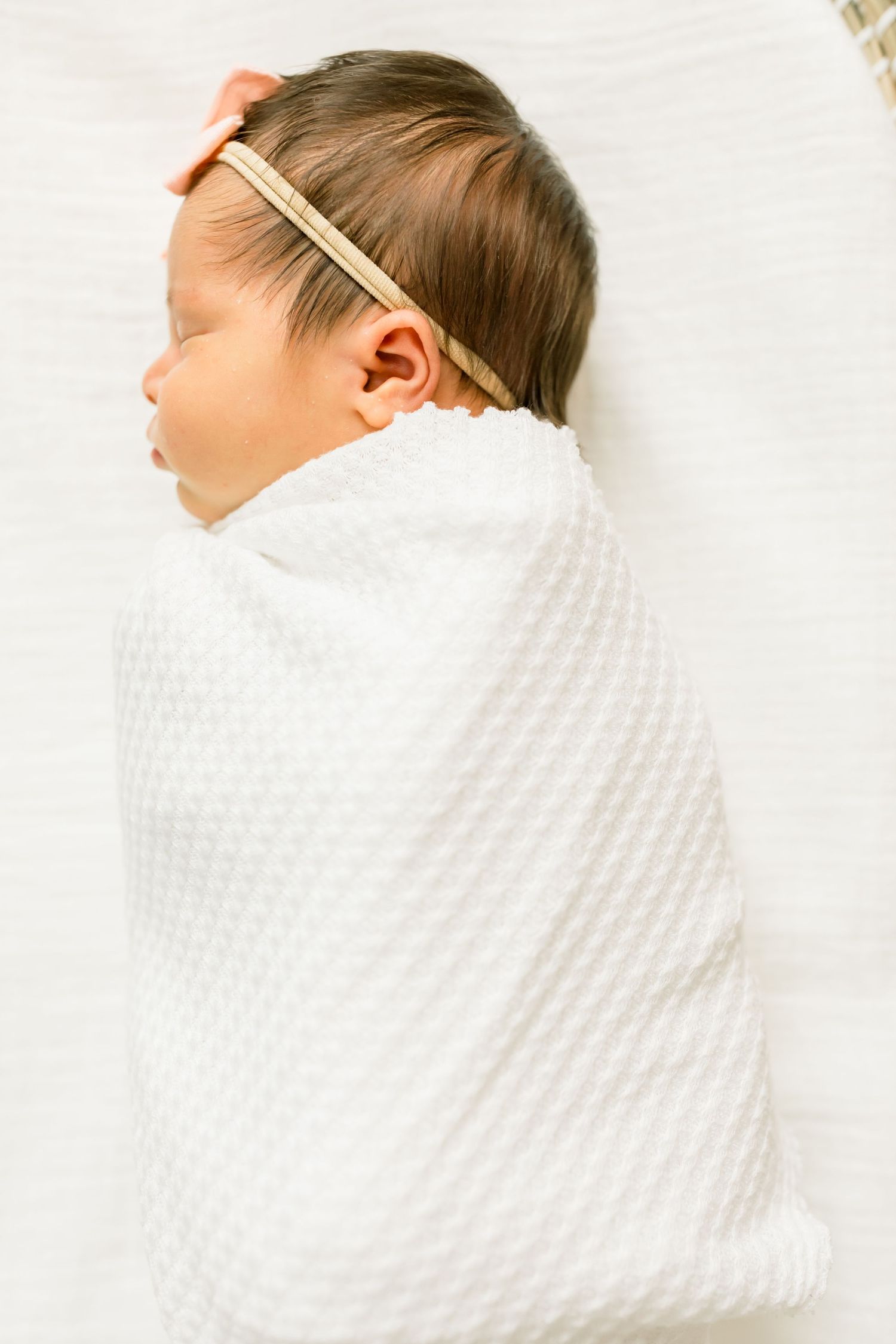 Swaddled newborn wearing neutral headband against white backdrop.