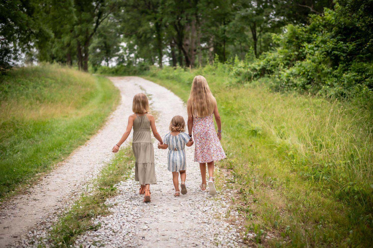 Three young children walking hand in hand down a scenic gravel path.