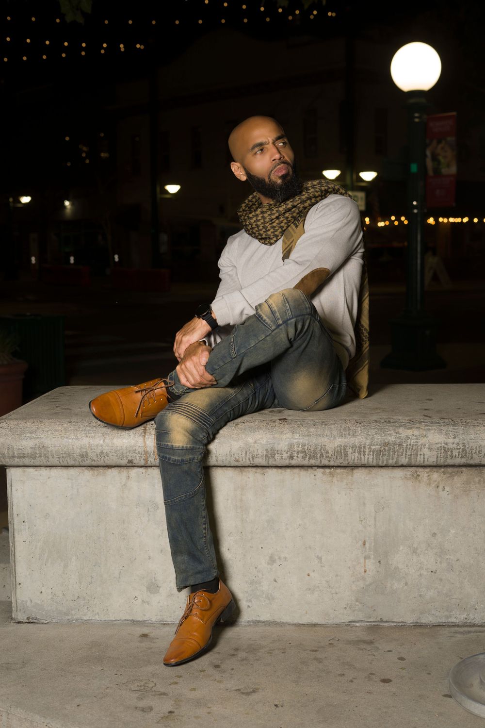 Male model in grey sweater and blue jeans position on brick wall for photoshoot
