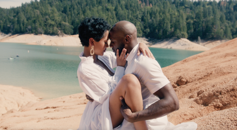 Couple on mountains intimately cuddles together with sand shore and blue water video shoot