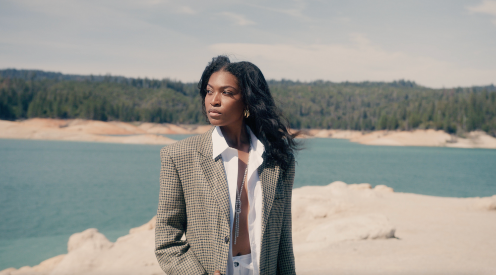 Fashion model on the lakeside with plaid coat and open dress shirt sticking a pose in video shoot